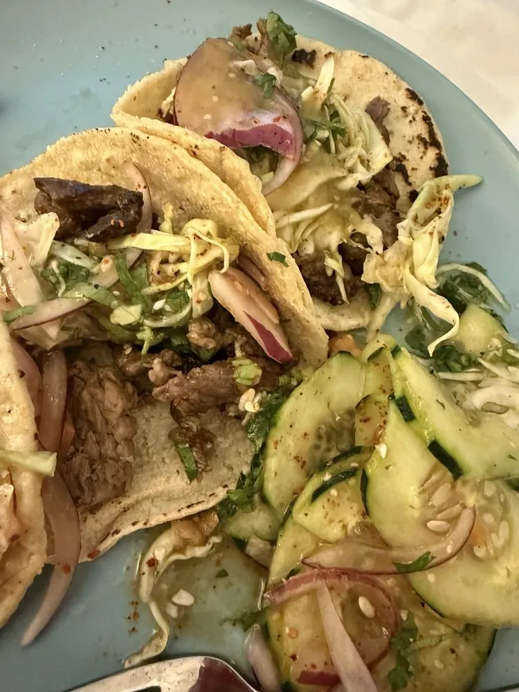 Tacos with onion and cabbage next to a cucumber salad