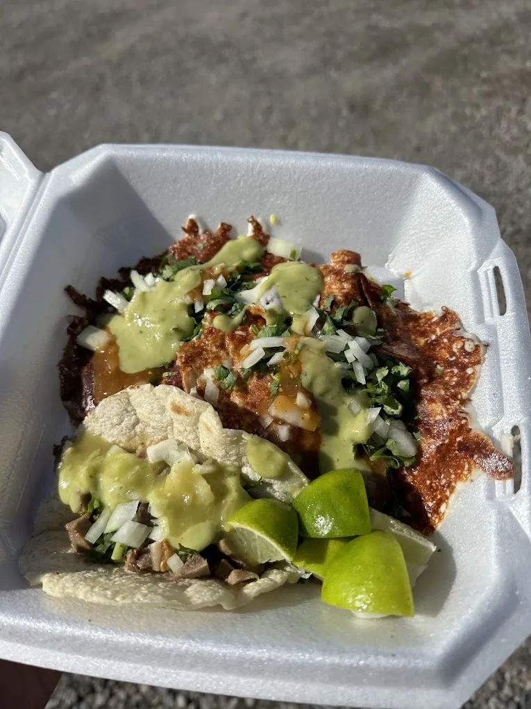 Tacos with green salsa, onion and lime wedges in a takeout box