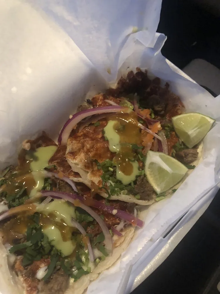 Tacos with green salsa, red onion and lime in a takeout tray