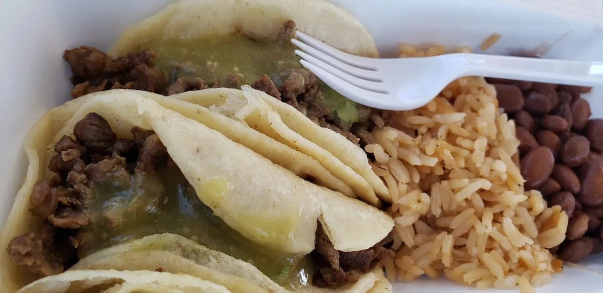 Tacos with green salsa next to rice and beans